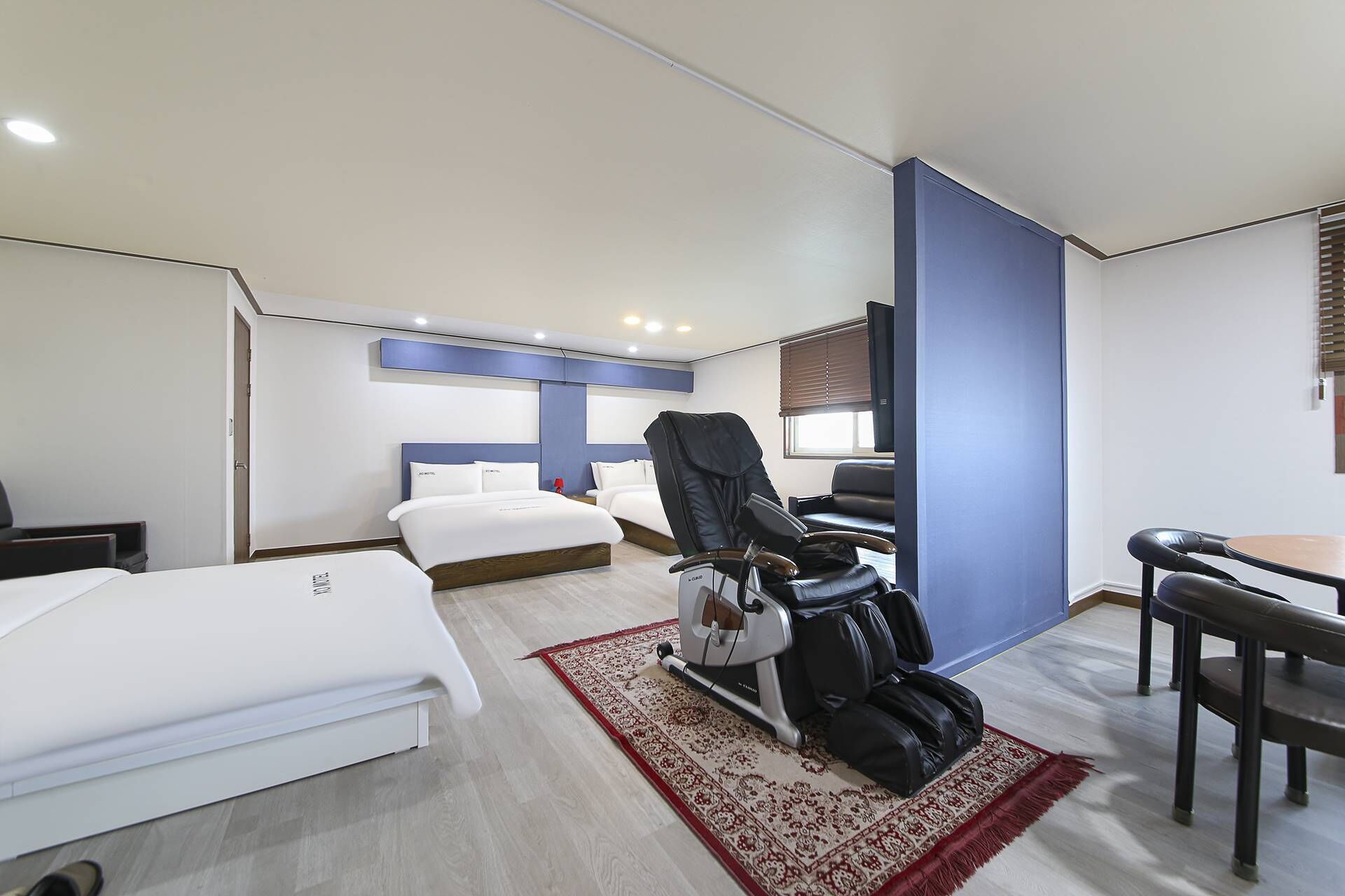 Una habitación de hotel con cama, sillón de masajes, escritorio y una silla.
