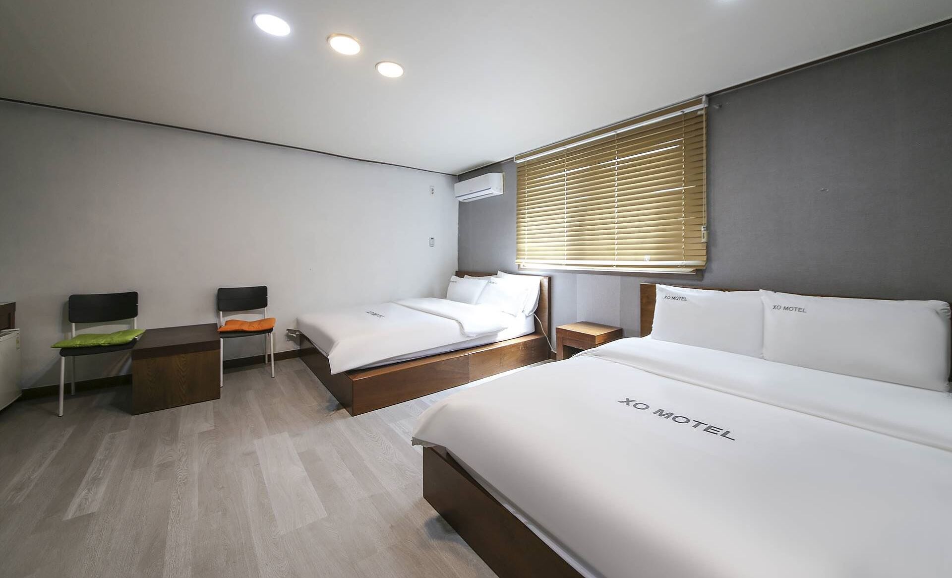 A hotel room with two beds, a desk, a chair, and a window with blinds.