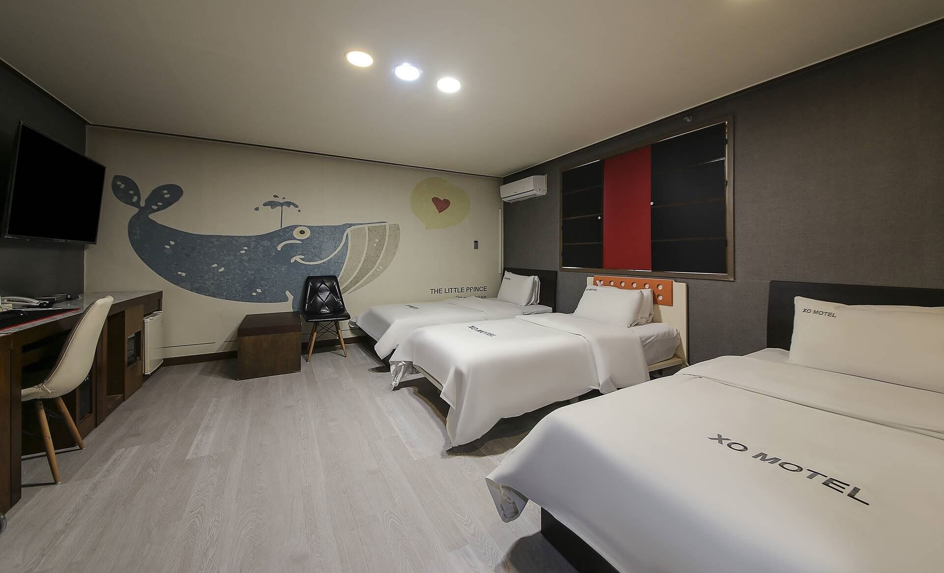 A hotel room with two beds, a desk, a chair, and a TV.