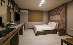 Un dormitorio con escritorio, cama, pared decorada con ladrillos y ventana con persianas.