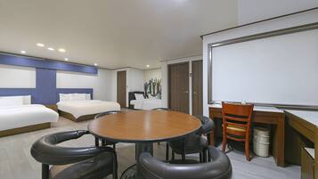 A hotel room with a large round table, two beds, a desk with a chair, and a whiteboard.