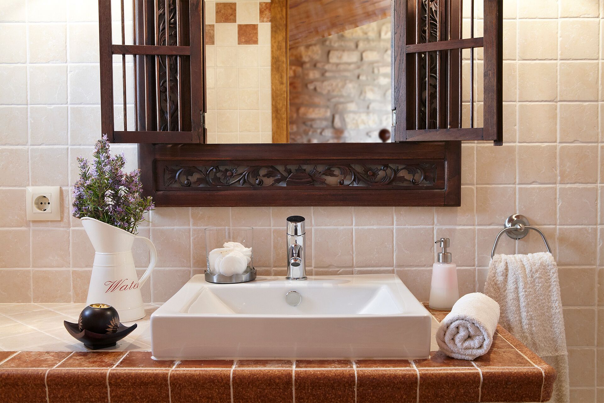 Un bagno con un lavandino bianco, uno specchio con cornice in legno, un vaso con fiori e un asciugamano.