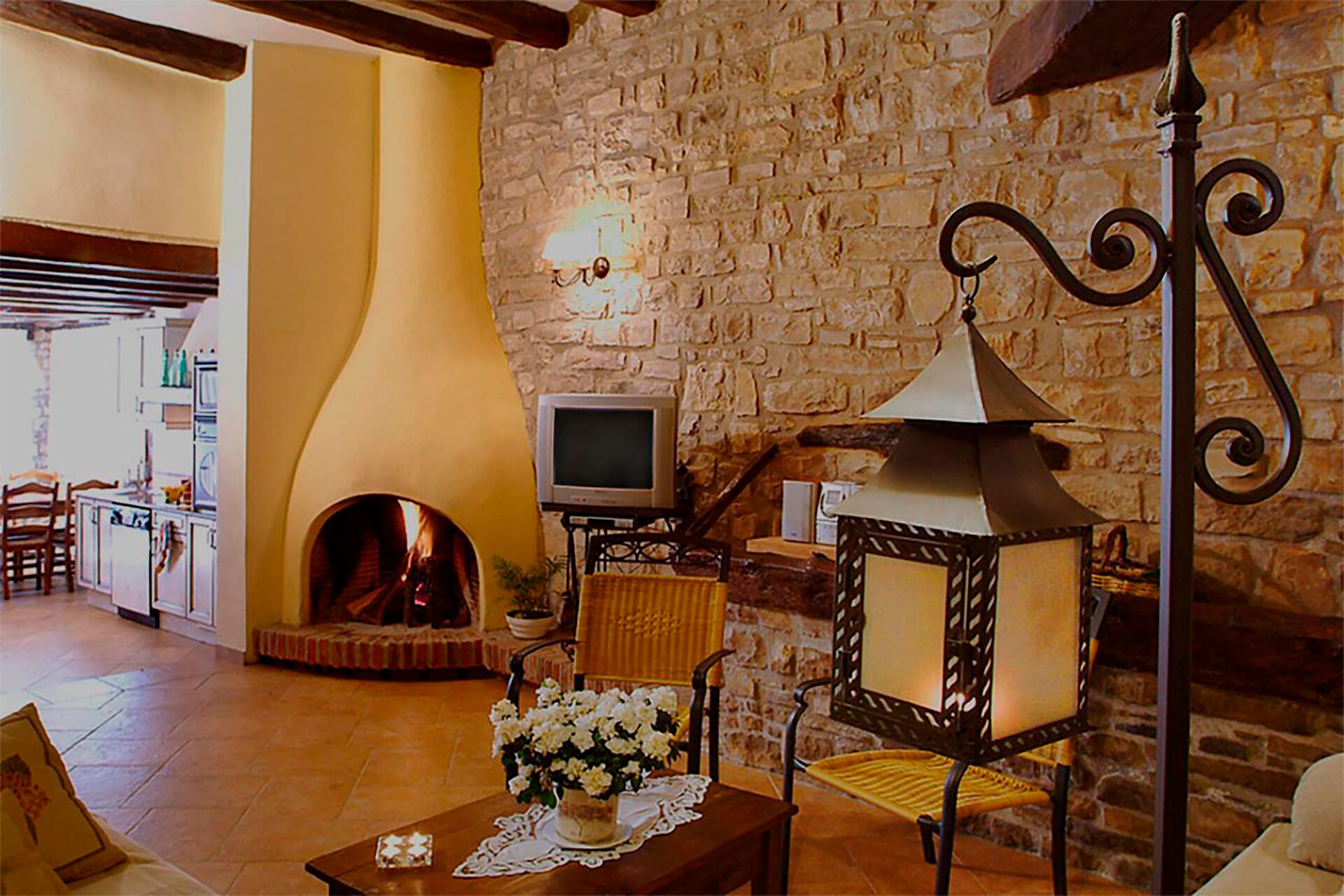 A cozy living room with a stone wall, a fireplace, a television, and a table with flowers.