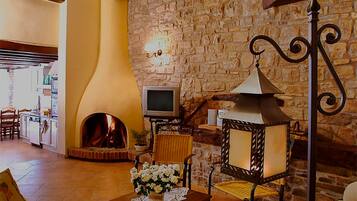 A cozy living room with a stone wall, a fireplace, a television, and a table with flowers.