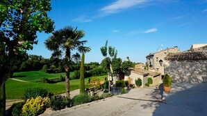 A rural setting with a stone building, lush greenery, and a clear blue sky. - Cal Carulla (Pujalt)