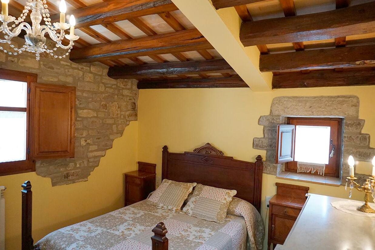 A bedroom with a wooden bed, stone walls, a stone fireplace, and a chandelier.