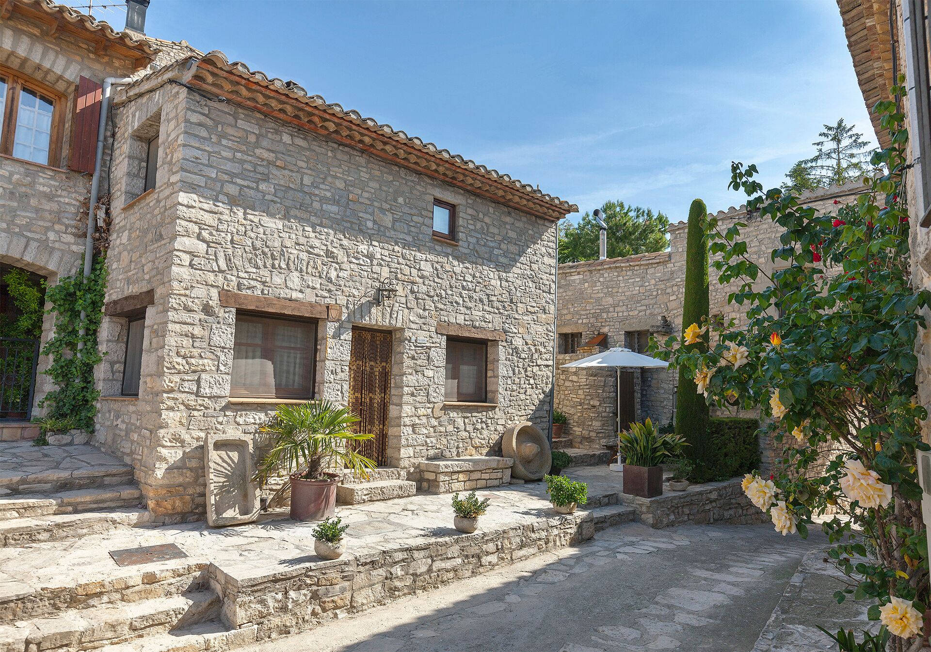A stone building with a tiled roof, a small window, and a door. There are steps leading to the entrance, and potted plants are placed around the area.