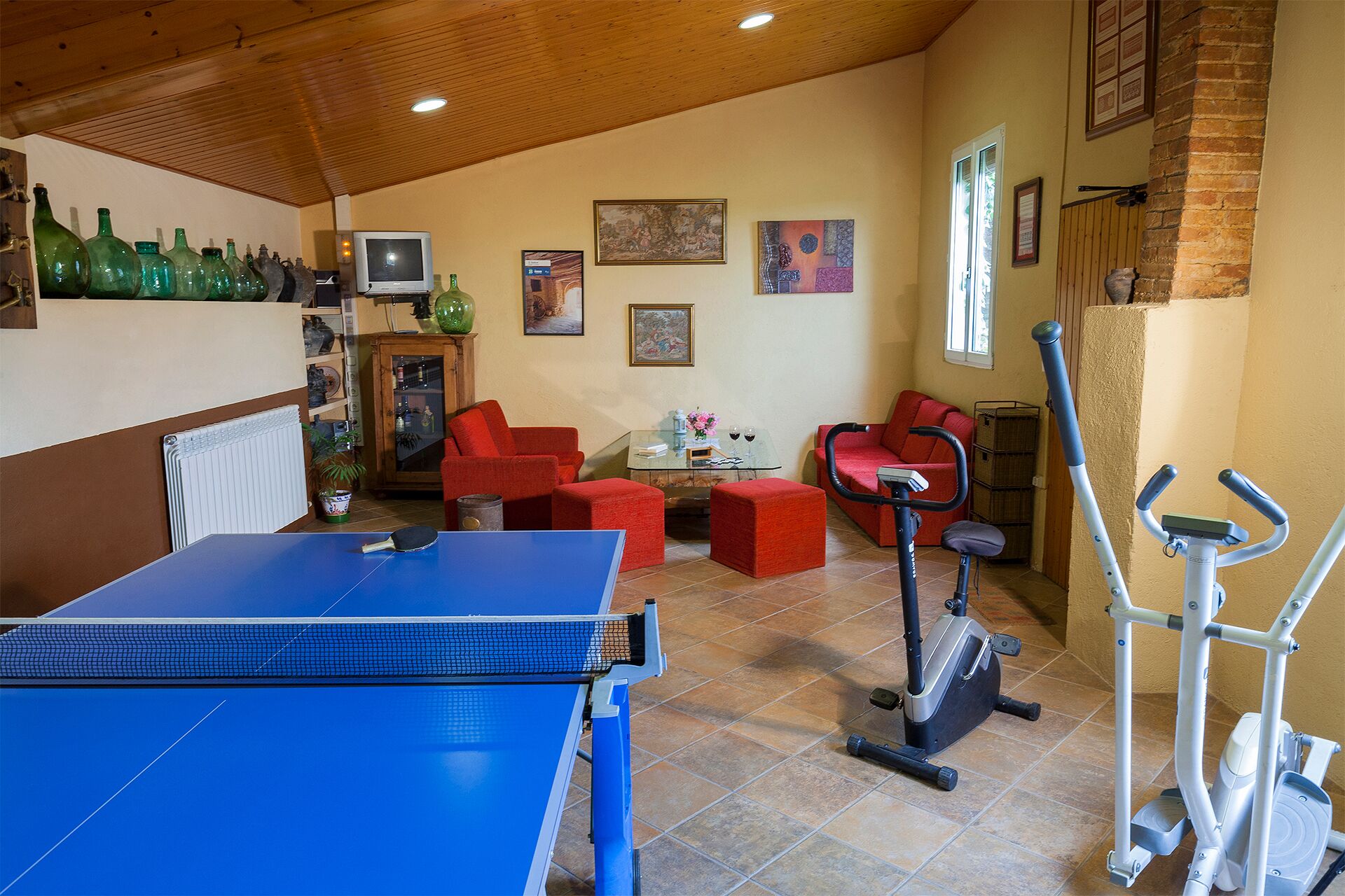 A room with a ping pong table, red sofas, exercise equipment, and various decorative items on the walls.