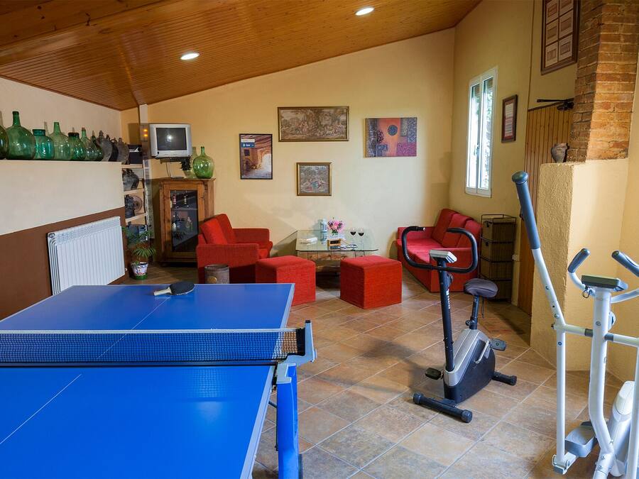 A room with a ping pong table, red sofas, exercise equipment, and various decorative items on the walls.