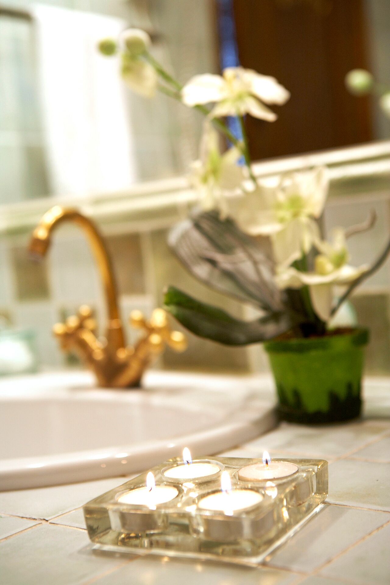 A bathroom with a sink, a gold faucet, and a green vase with white flowers.