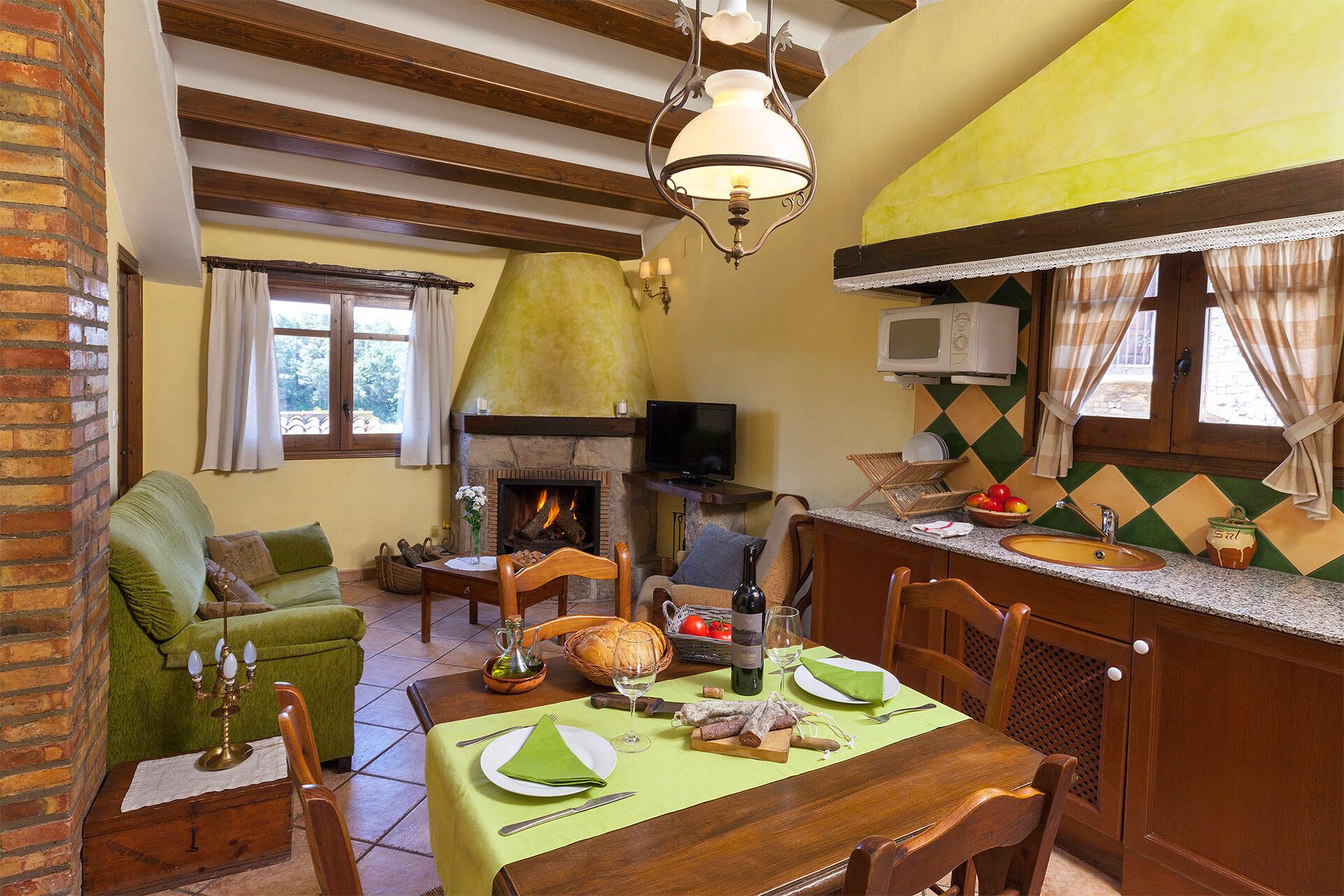 A cozy living room with a fireplace, a dining table set for two, and a kitchen area with a microwave and sink.
