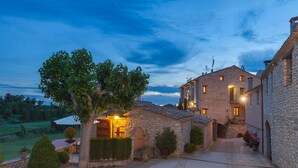 A stone building with a courtyard, a tree, and a well-lit entrance. - Cal Carulla (Pujalt)