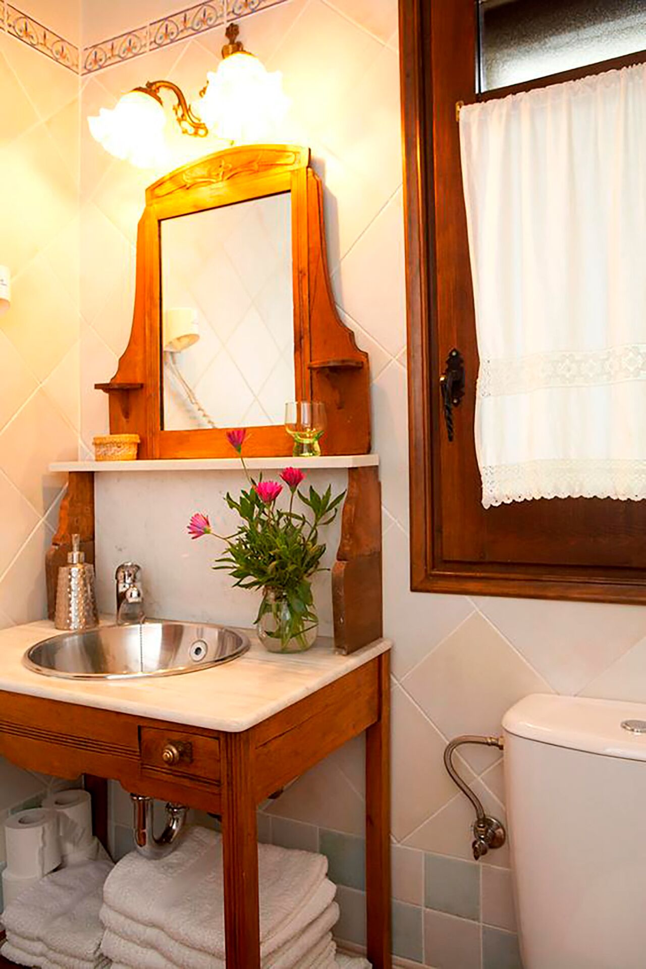 Un baño con tocador de madera, lavabo, espejo, inodoro y toallero.