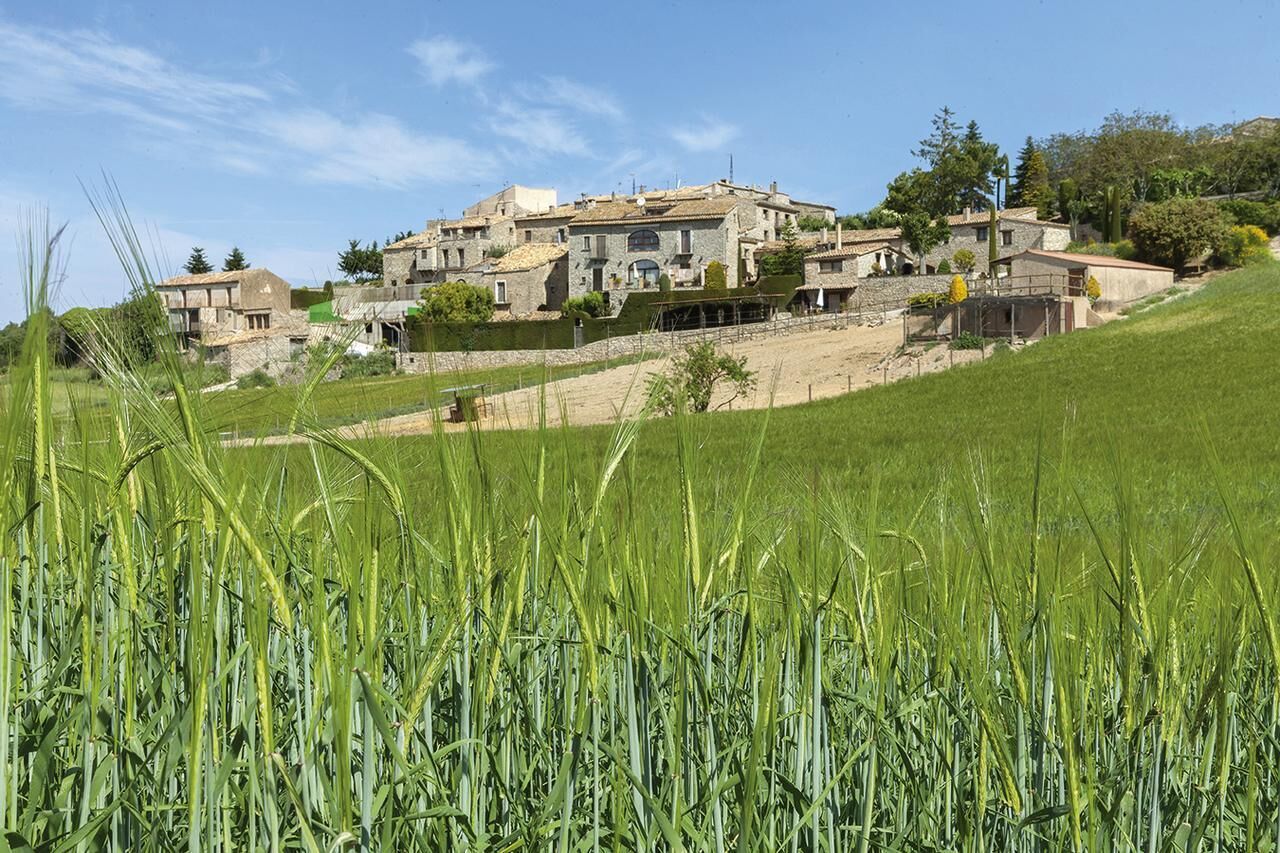 Un pueblo rural con edificios de piedra, un campo cubierto de hierba y un cielo despejado.