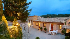 A stone building with a tiled roof, outdoor seating, and potted plants. - Cal Carulla (Pujalt)