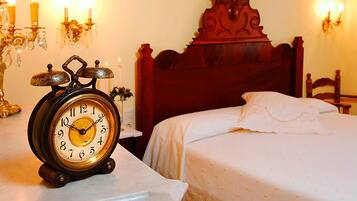 Een klassiek houten bed met witte beddengoed, een vintage wekker op een nachtkastje, en wandklemmen met kaarsen.