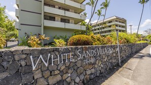 A multi-story building with a stone wall in front labeled "WHITE SANDS VILLAGE" and a phone number. - Summer Deal White Sands Beach Condo with Pool Lanai and Ocean Views (Kailua Kona)