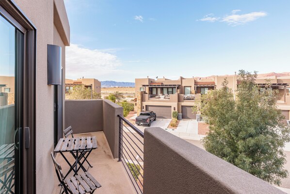 A balcony with a table and chairs, a parked truck, and a view of neighboring buildings and a tree.