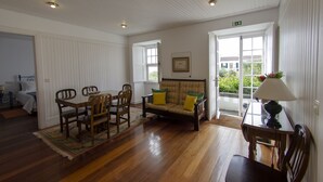 A room with a wooden floor, a sofa with yellow cushions, a dining table with chairs, and a lamp. - Quinta das Buganvílias (Horta)