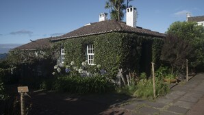 A house with a tiled roof, surrounded by lush greenery and a clear sky. - Quinta das Buganvílias (Horta)
