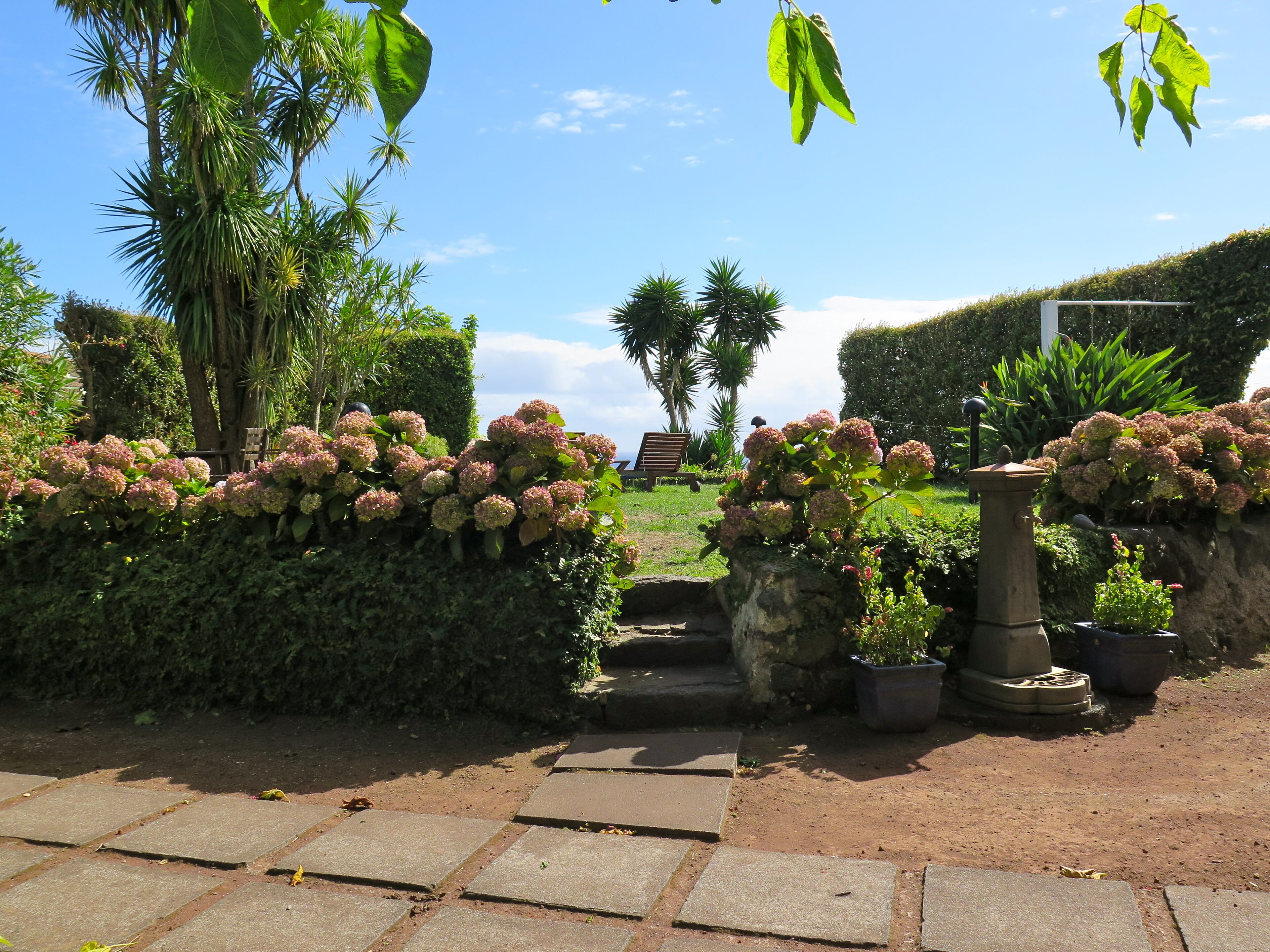 A garden pathway with stone tiles leading to a seating area with a bench and a small table.