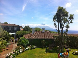 A garden with a pathway, benches, and a view of a mountain and ocean. - Quinta das Buganvílias (Horta)