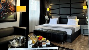 Quarto de hotel moderno com uma cama grande, um sofá, uma mesa de jantar e uma bolsa Louis Vuitton, além de uma pintura decorativa de borboleta.