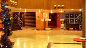 Um hall amplo com piso reluzente, balcão de recepção, escada e um pinheiro de Natal com luzes.