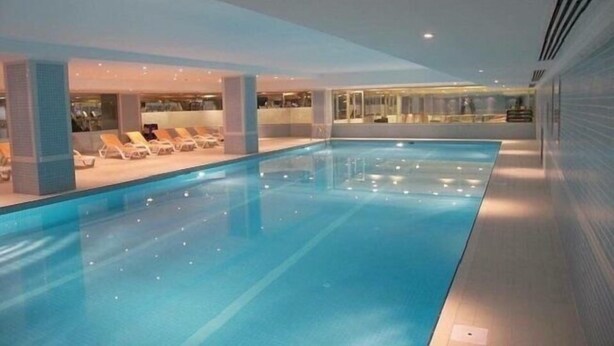 Piscina interna com espreguiçadeiras e parede de vidro.