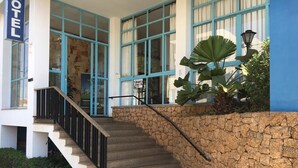 Entrada de hotel con un muro de piedra, una escalera y una planta grande.