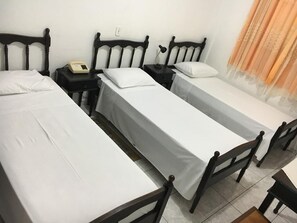 A hotel room with three single beds, each with a wooden headboard and white bedding. There is a bedside table with a lamp and a telephone on one side. - Hotel Itararé (Itarare)