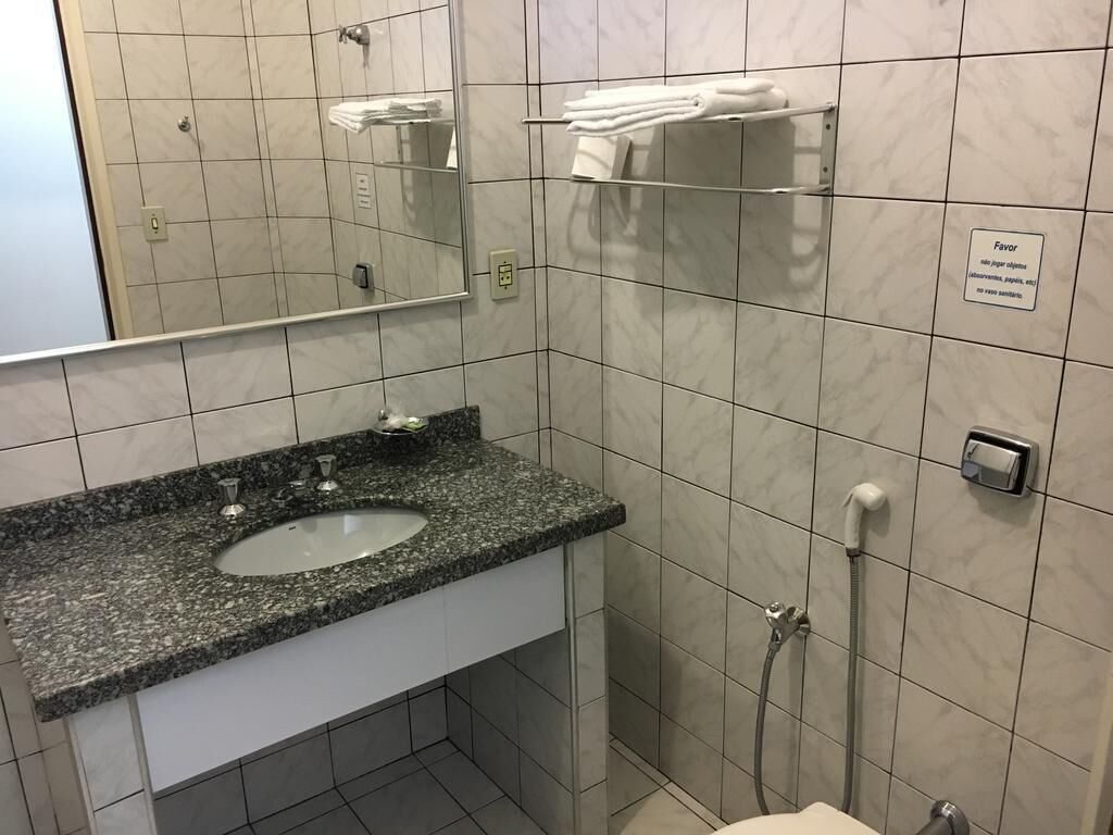 A bathroom with a granite countertop sink, a mirror, a towel rack, and a shower.