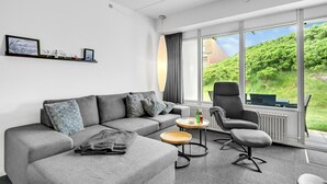 A modern living room with a grey sofa, a grey armchair, and a small round table. There is a large window with a view of greenery outside. - Awesome apartment in Ringkøbing (Ringkøbing)