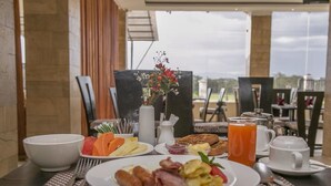 A breakfast table with plates of food, a vase of flowers, and a glass of orange juice. - The Nest Boutique Hotel (Naivasha)