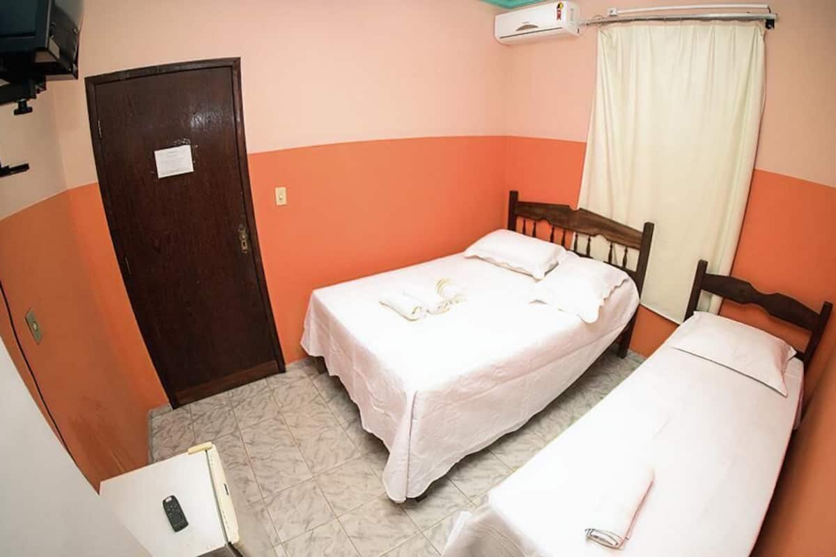 A small, single-room hotel with two beds, a wooden door, and a white air conditioning unit.