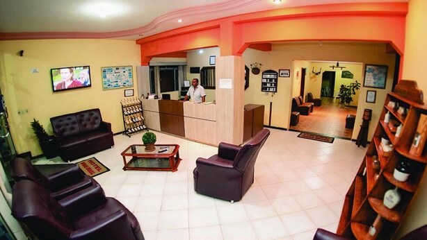 A hotel lobby with leather sofas, a reception desk, a coffee table, and a wooden bookshelf. - Minas Brasil Hotel (Salinas)