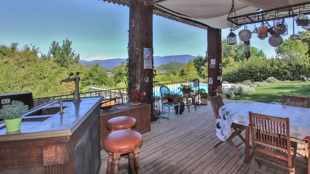 Una terraza de madera con zona de bar, asientos al aire libre y vistas a montañas.