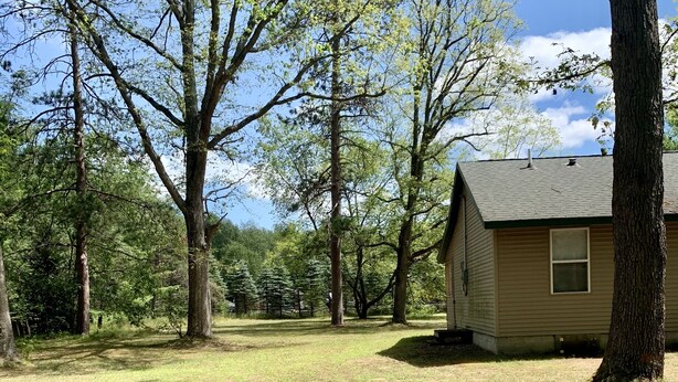 Une petite cabane avec un toit en pente, entourée d’une zone herbeuse et d’arbres.
