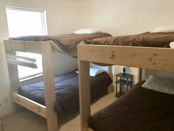Une chambre de dortoir équipée de deux lits superposés, d’une petite table et d’une fenêtre laissant entrer la lumière naturelle.