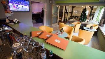 Zona de bar con mostrador, vasos y una televisión mostrando un evento deportivo.