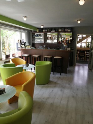 A bar area with stools, a counter with bottles, and a view of the outside. - Memory Hotel & Restaurant (Braunlage)