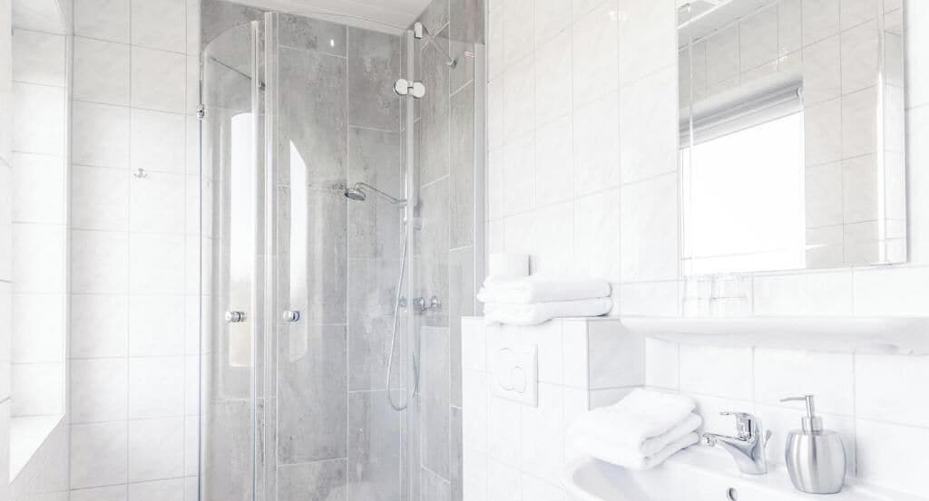Une salle de bain moderne avec une douche à parois de verre, un lavabo blanc et un miroir au-dessus du lavabo.