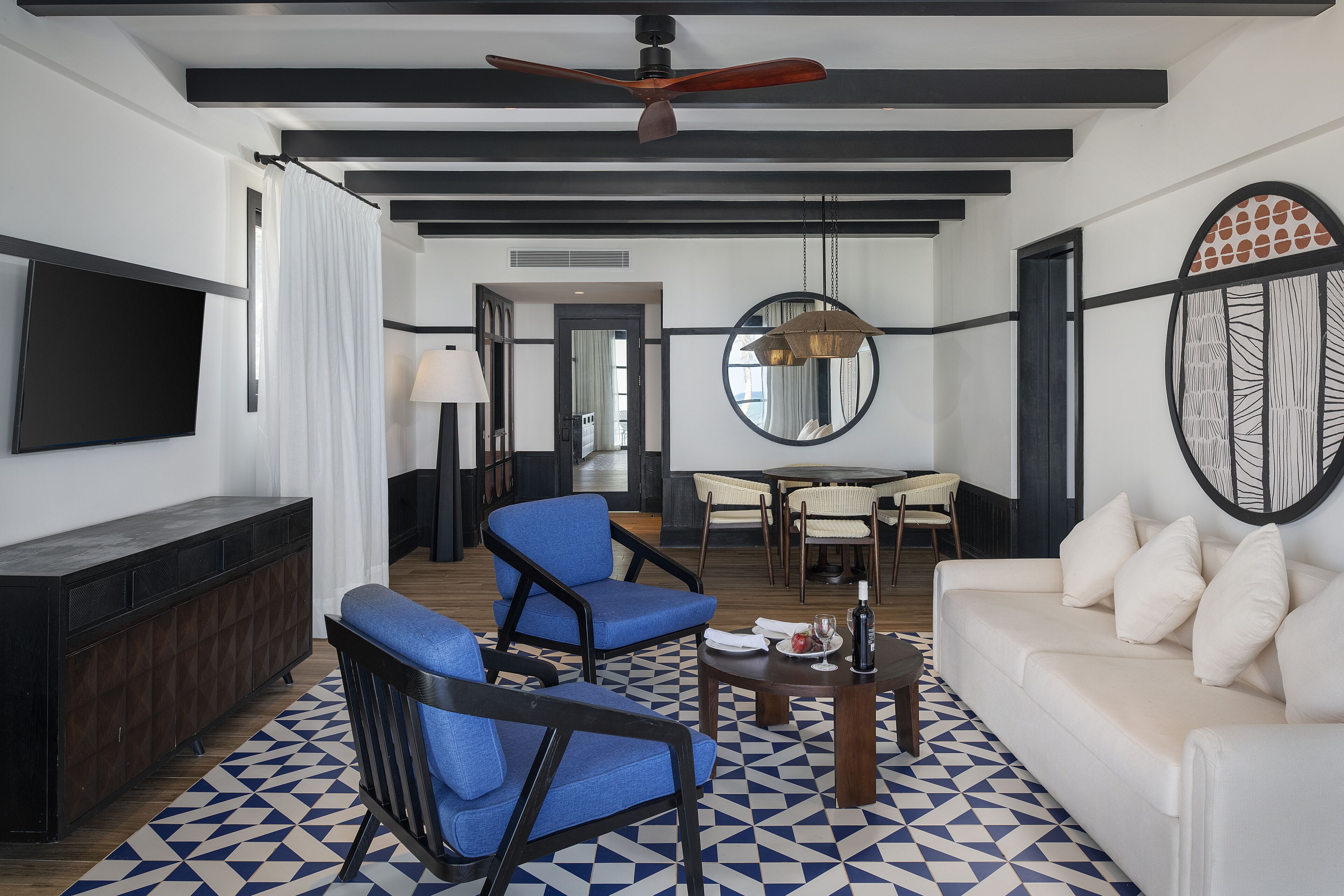 Un salon moderne avec un canapé, des fauteuils bleus, une table basse et un téléviseur.