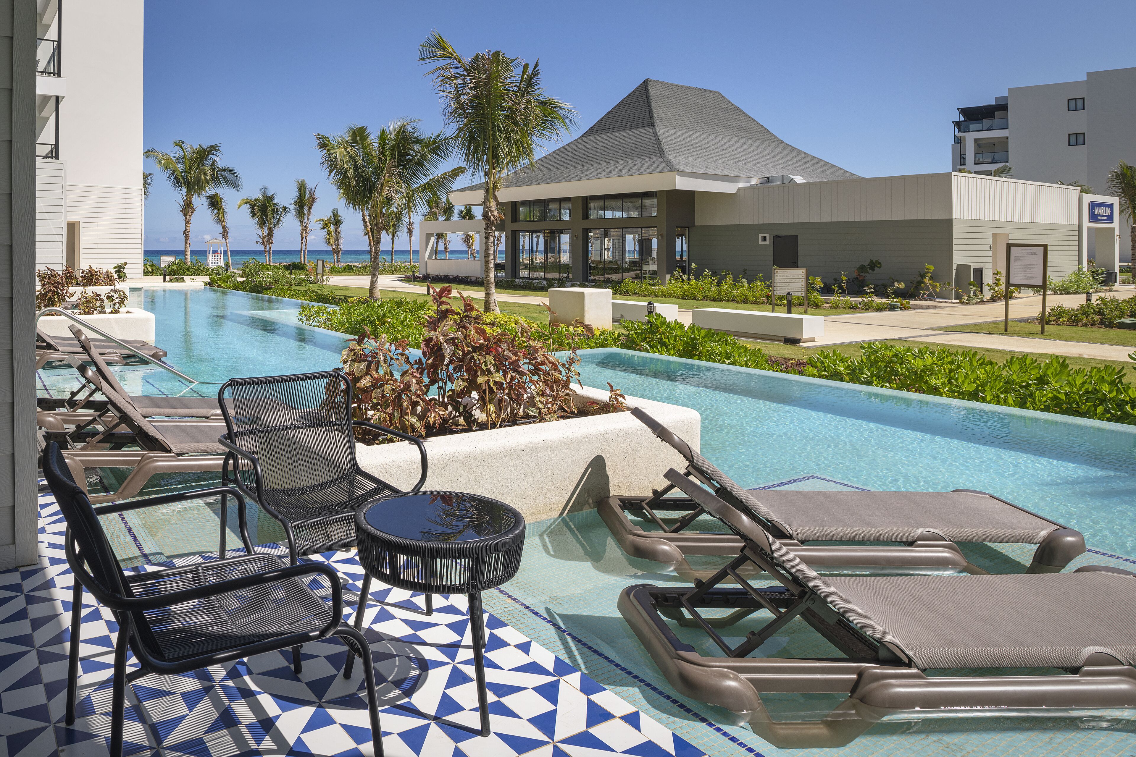 Zona de piscina con sillones de descanso y una pequeña mesa, rodeada de vegetación y una vista despejada del océano.