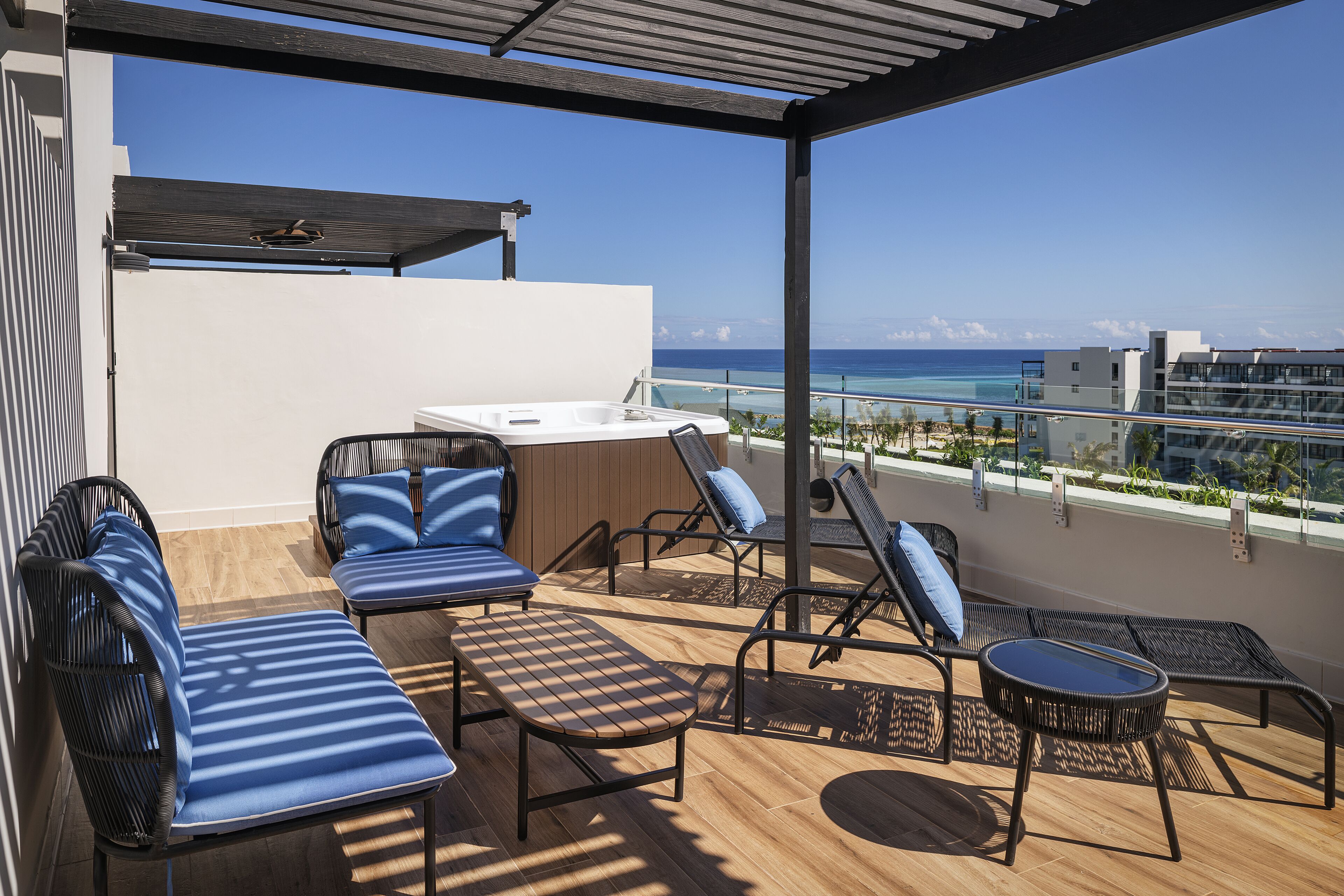 A rooftop terrace with lounge chairs, a hot tub, and a view of the ocean.
