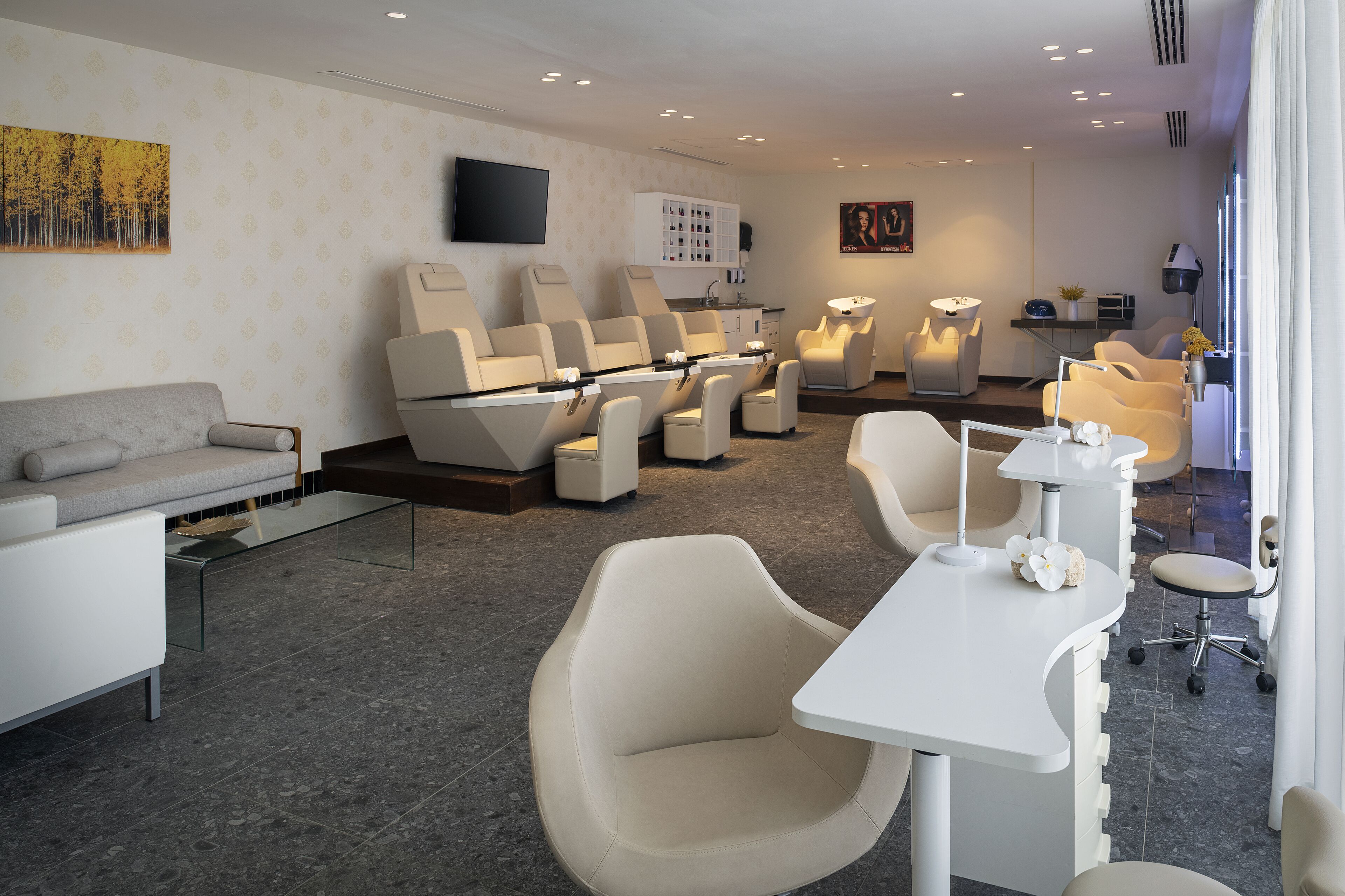 A modern spa room with a sofa, massage chairs, a massage table, and a reception desk.