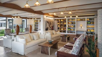 A spacious living area with a large sofa set, a coffee table, and a patterned armchair. There are multiple bookshelves filled with books and decorative items.