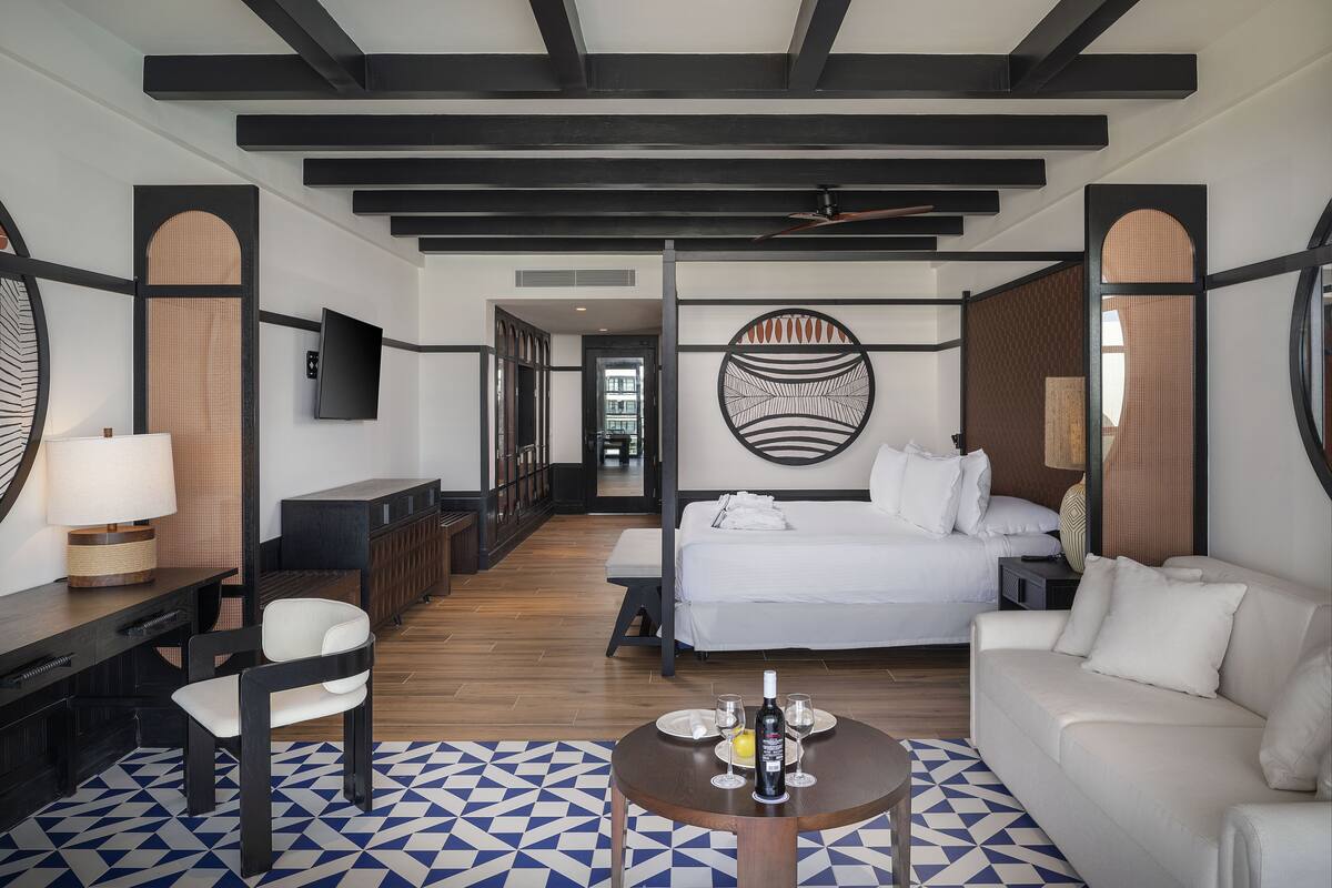 A modern hotel room with a bed, sofa, desk, and TV.