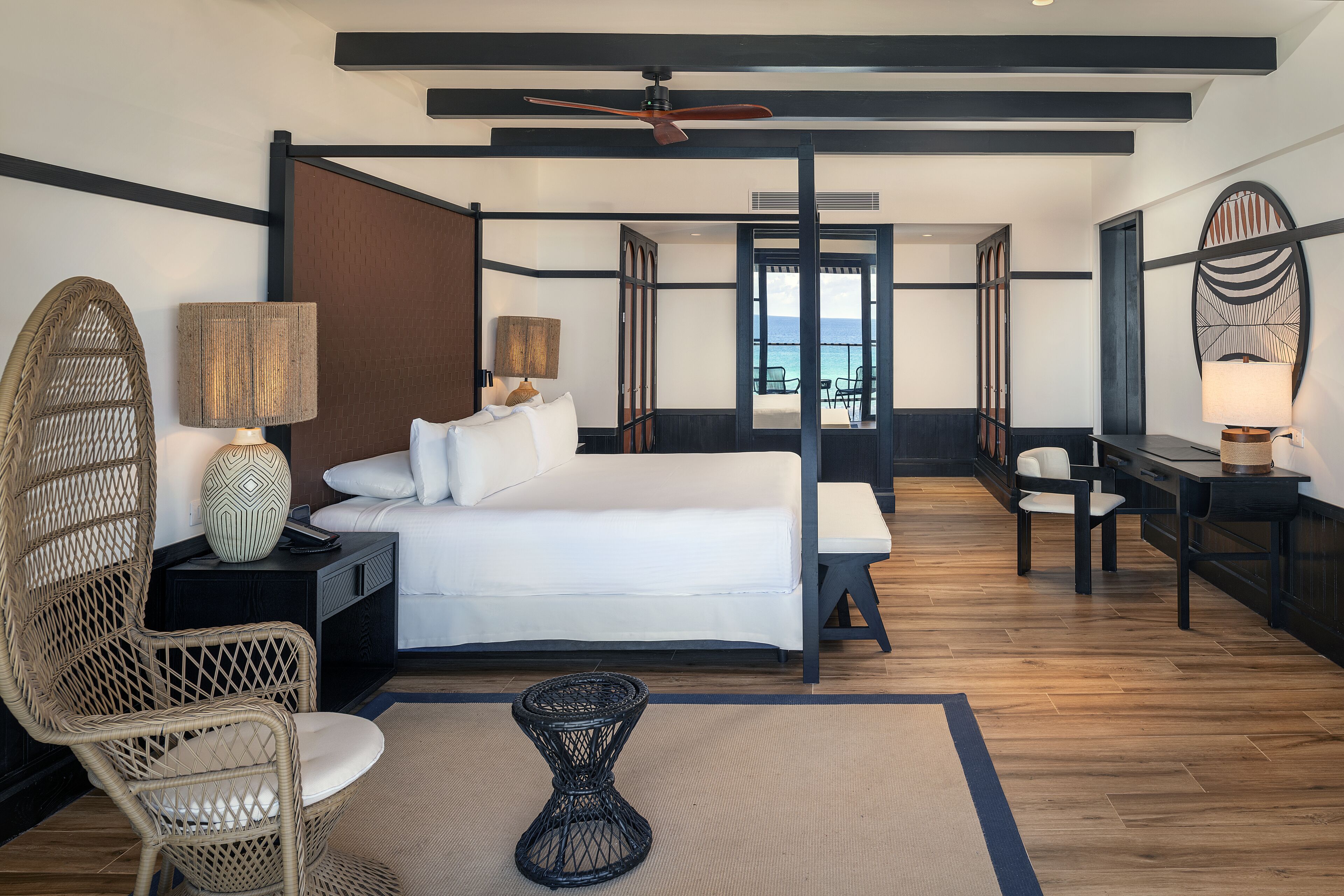 A modern hotel room with a bed, a chair, a desk, and a view of the ocean.