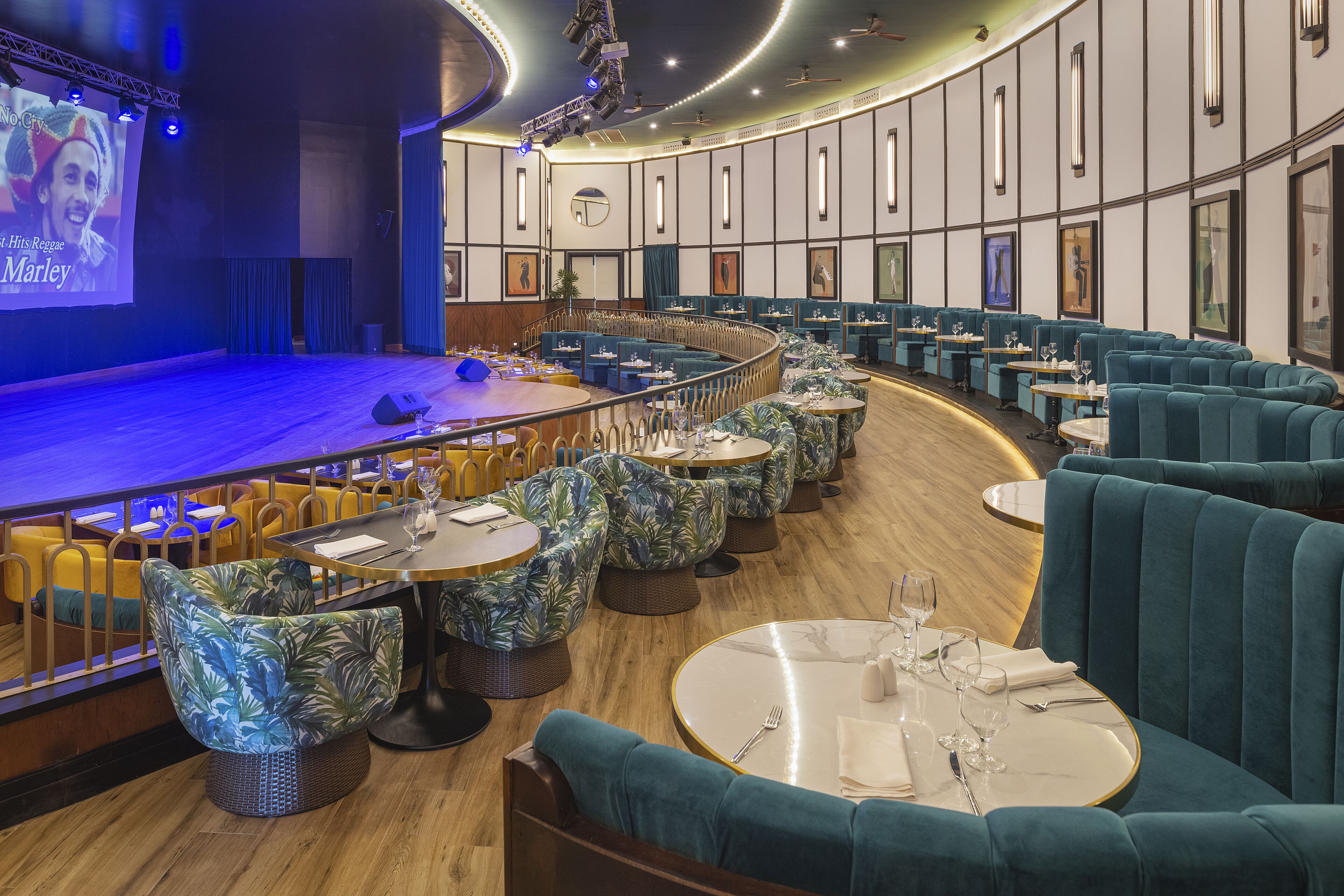 A restaurant with a stage, round tables, and teal upholstered seating.